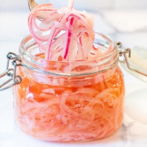 a mason jar of pickled onions with a fork pulling some out.