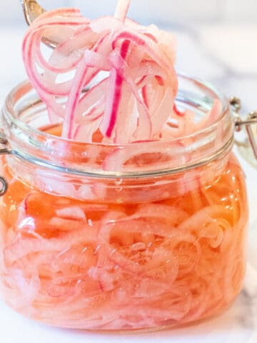 a mason jar of pickled onions with a fork pulling some out.