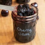 an open jar of labeled cherry jam with a knife taking some out.