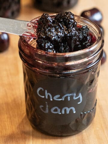 an open jar of labeled cherry jam with a knife taking some out.