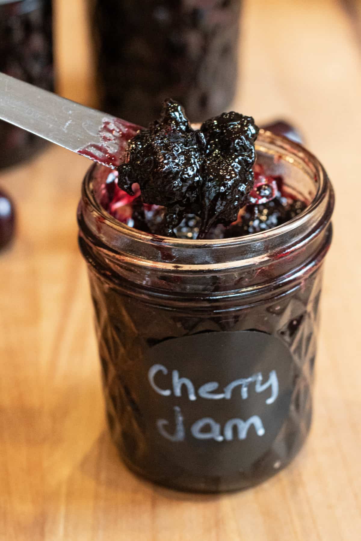 an open jar of labeled cherry jam with a knife taking some out.