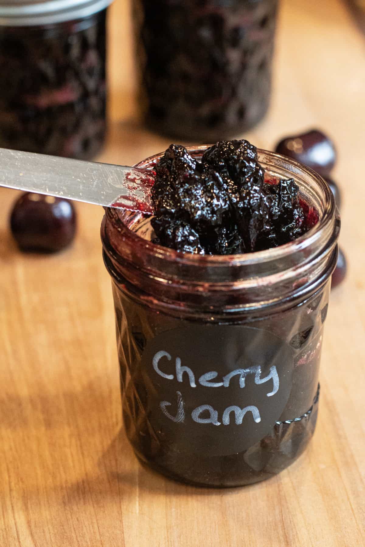 an open jar of labeled cherry jam with a knife taking some out.