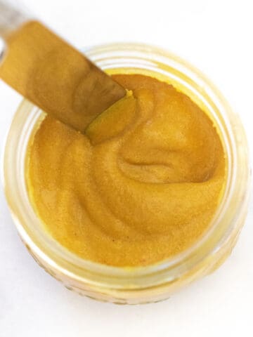an overhead of a jar of yellow mustard with a knife in it.