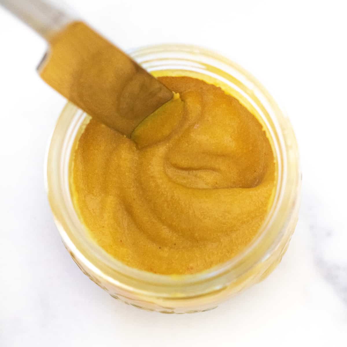 an overhead of a jar of yellow mustard with a knife in it.