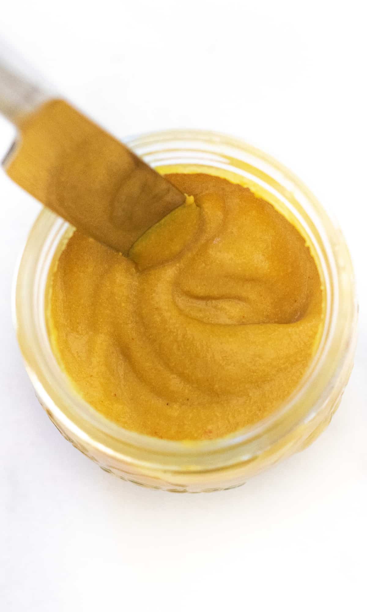 an overhead of a jar of yellow mustard with a knife in it.