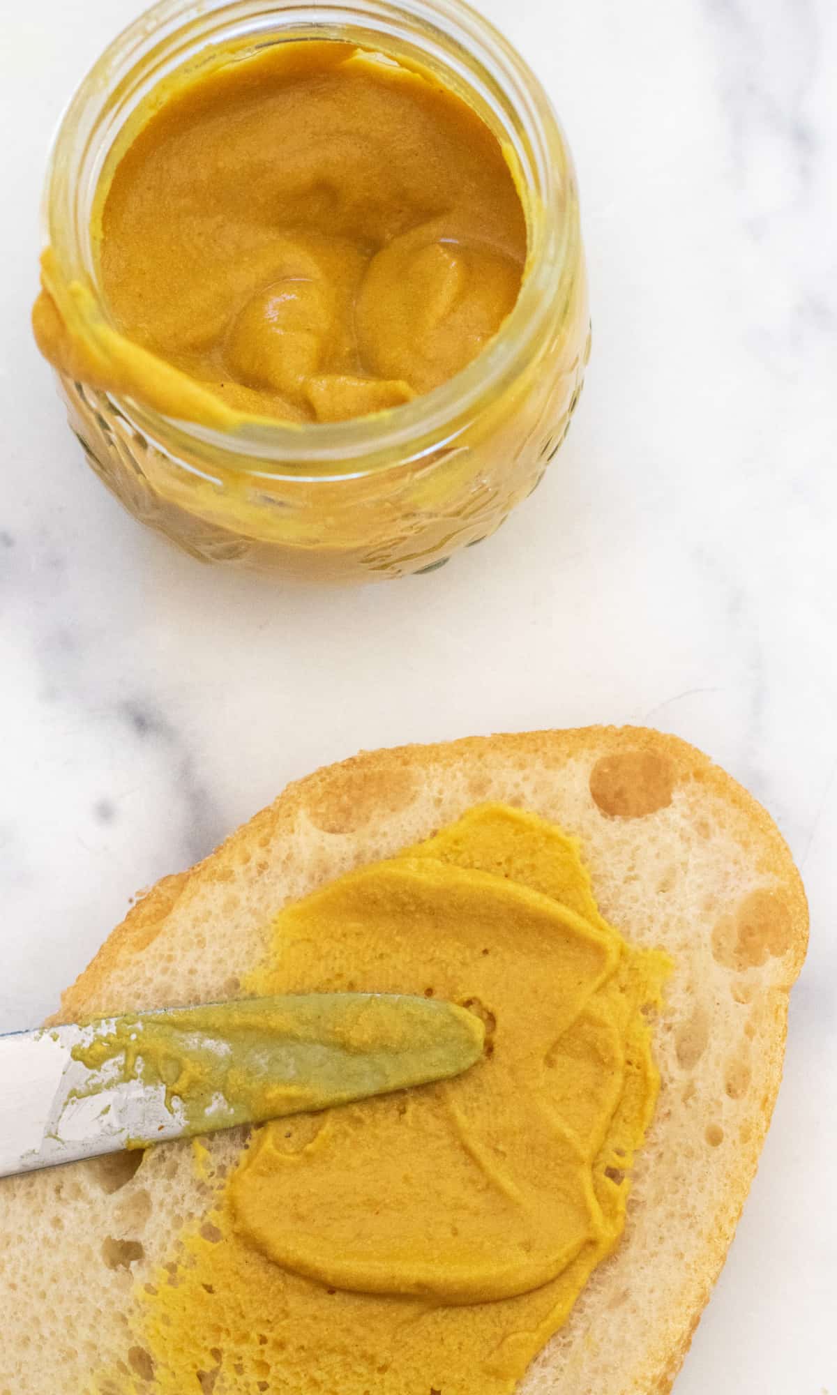 a knife of mustard spreading it on some bread.