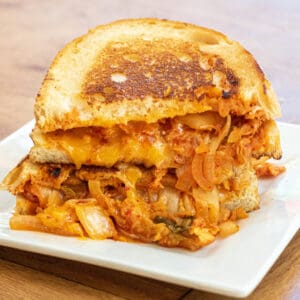 a stacked grilled cheese with onions and kimchi on a plate.