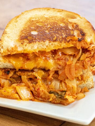 a stacked grilled cheese with onions and kimchi on a plate.