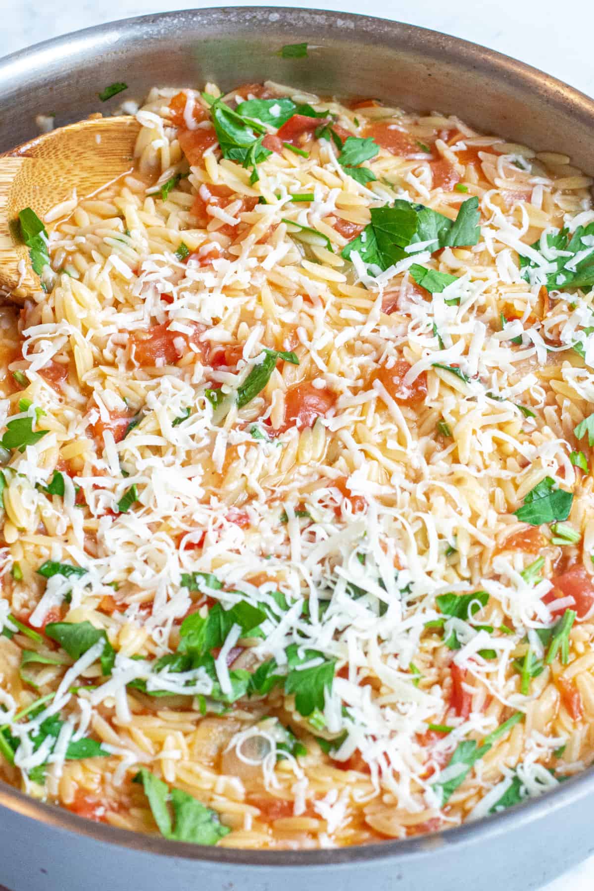 a pot of orzo with tomatoes, cheese, and parsley.