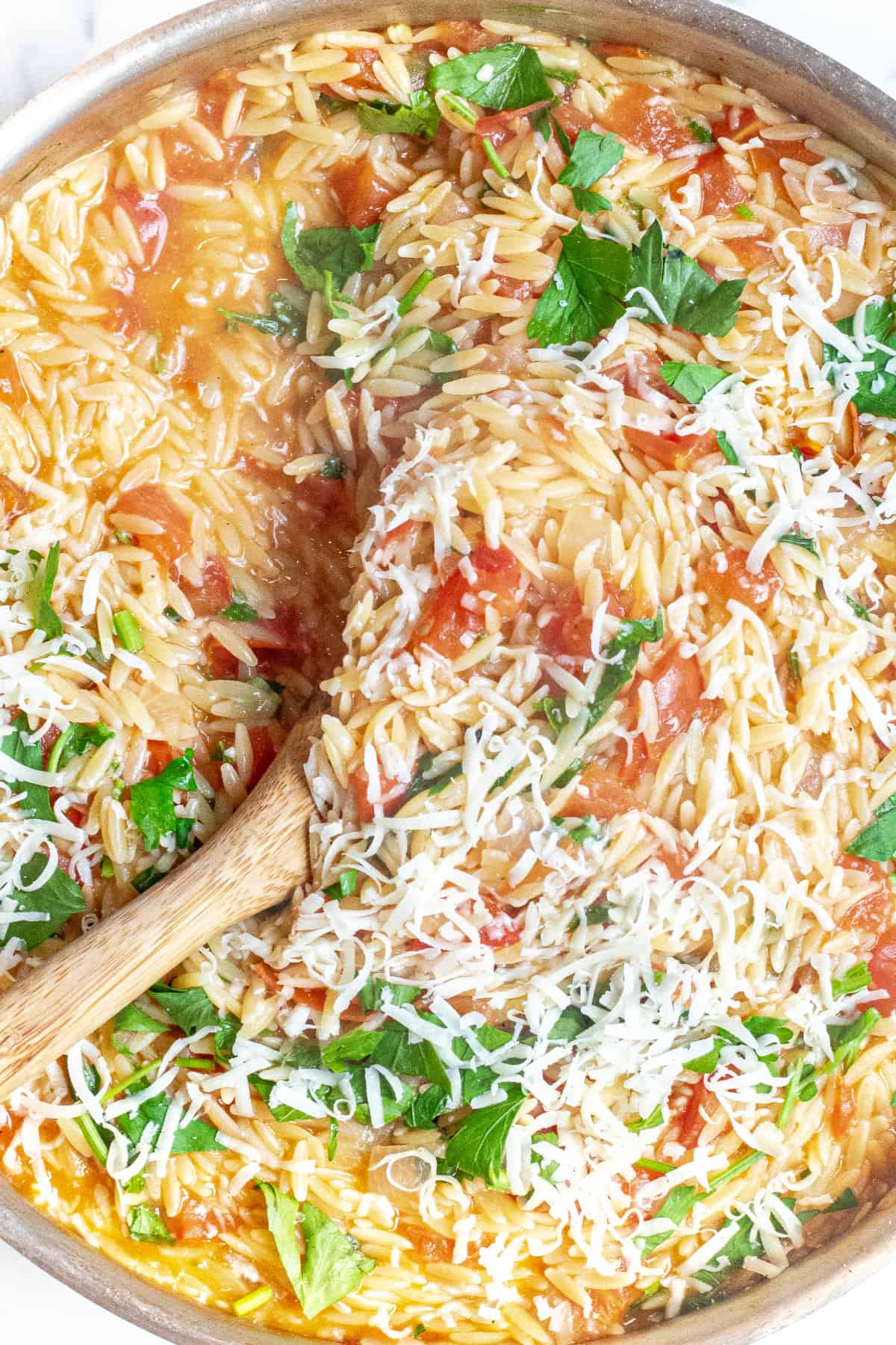 a pot of orzo with tomatoes, cheese, and parsley.