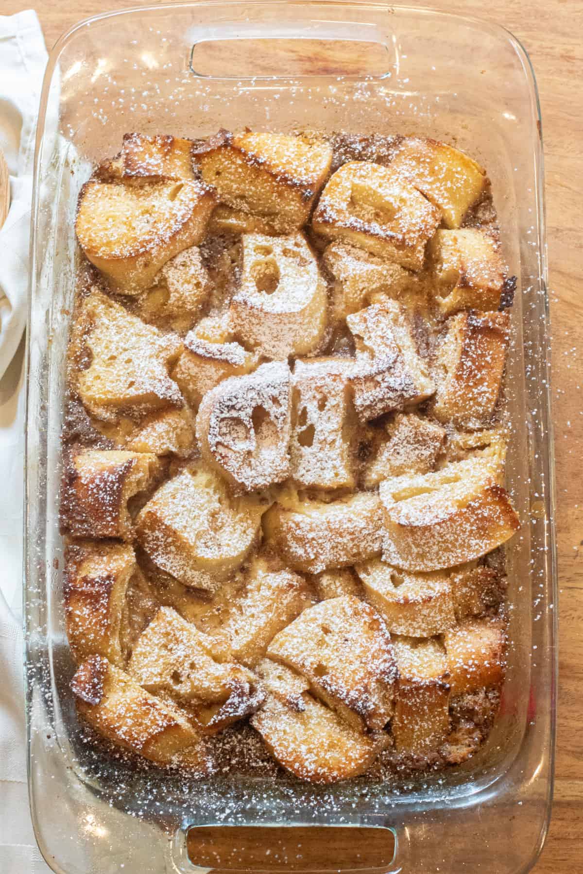 an overhead of a pan of bread pudding next to a wooden spoon.