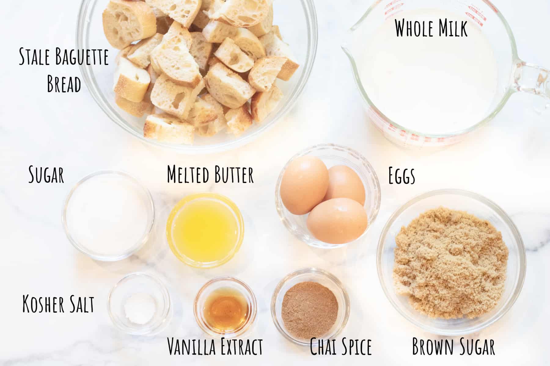 cubed bread, milk, sugars, eggs, melted butter, vanilla extract, and chai spice in bowls and labeled. 