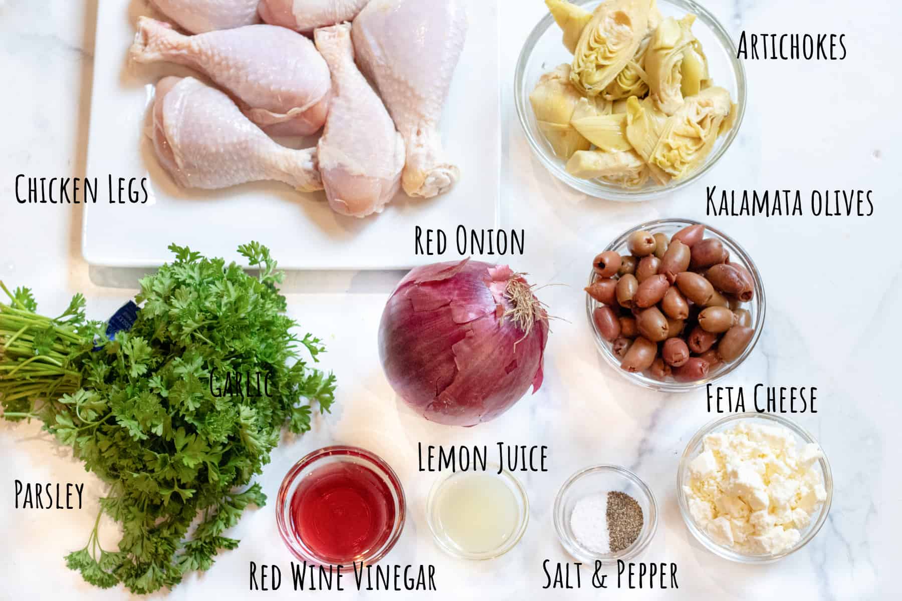 a plate of chicken legs, and bowls of artichokes, olives, feta, vinegar, salt and pepper, lemon juice, parsley, and a red onion.