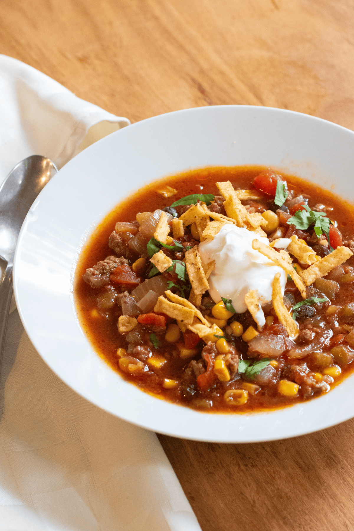 a large bowl of soup with corn, ground beef, and topped with sour cream and tortilla chips.