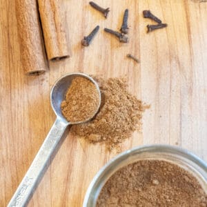 a teaspoon of pumpkin pie spice with cinnamon sticks, cloves, a jar, and ginger.