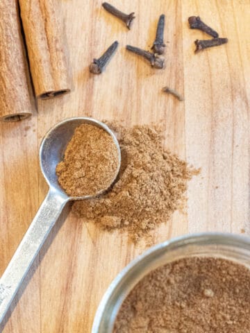 a teaspoon of pumpkin pie spice with cinnamon sticks, cloves, a jar, and ginger.