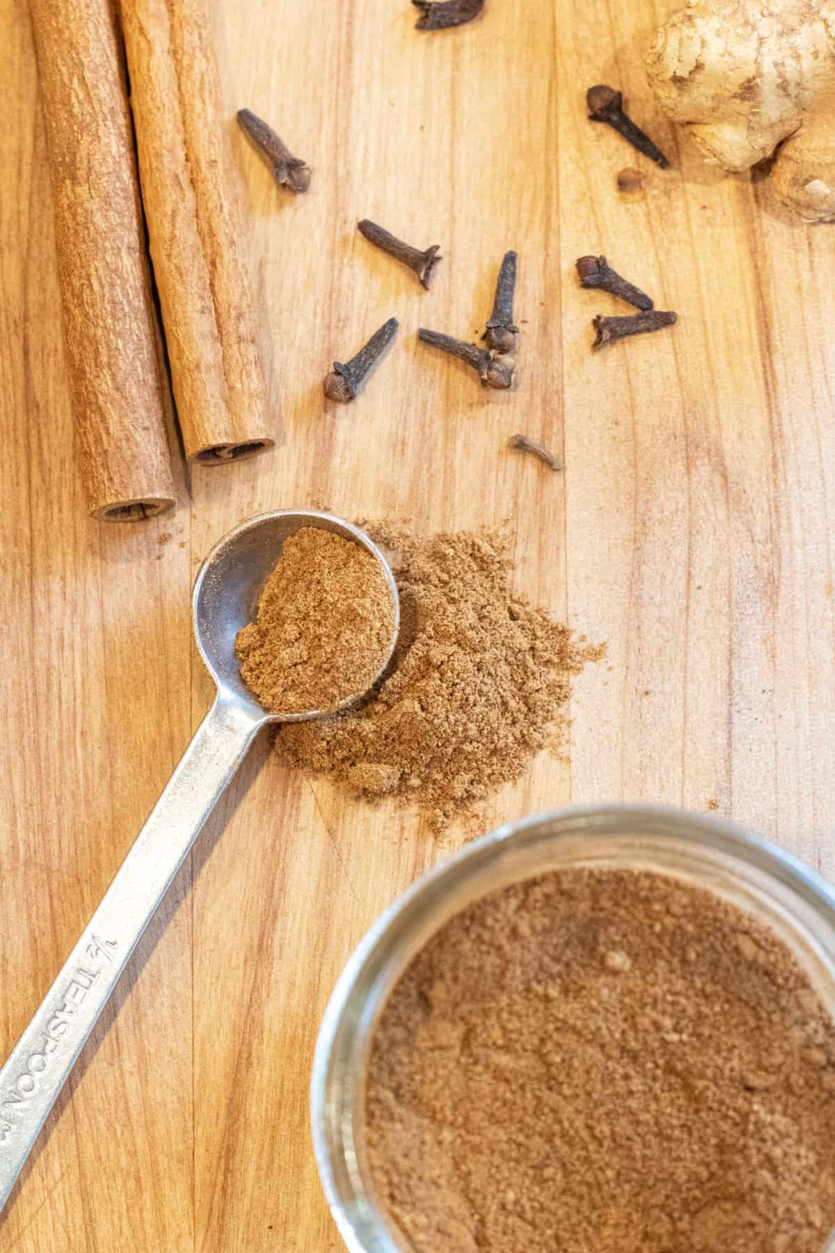 a teaspoon of pumpkin pie spice with cinnamon sticks, cloves, a jar, and ginger.