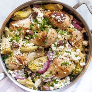 a pan of chicken legs, olives, artichokes, and feta cheese.