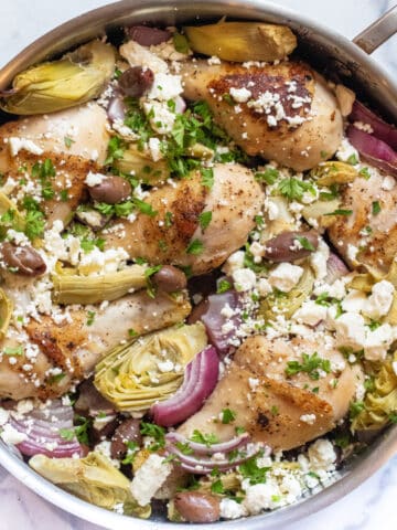 a pan of chicken legs, olives, artichokes, and feta cheese.