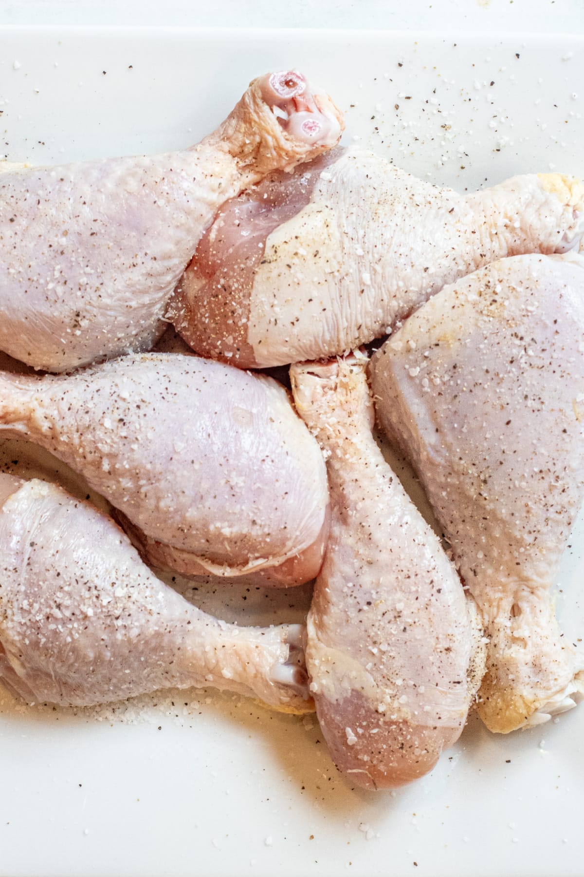 a plate of raw chicken legs seasoned with salt and pepper.