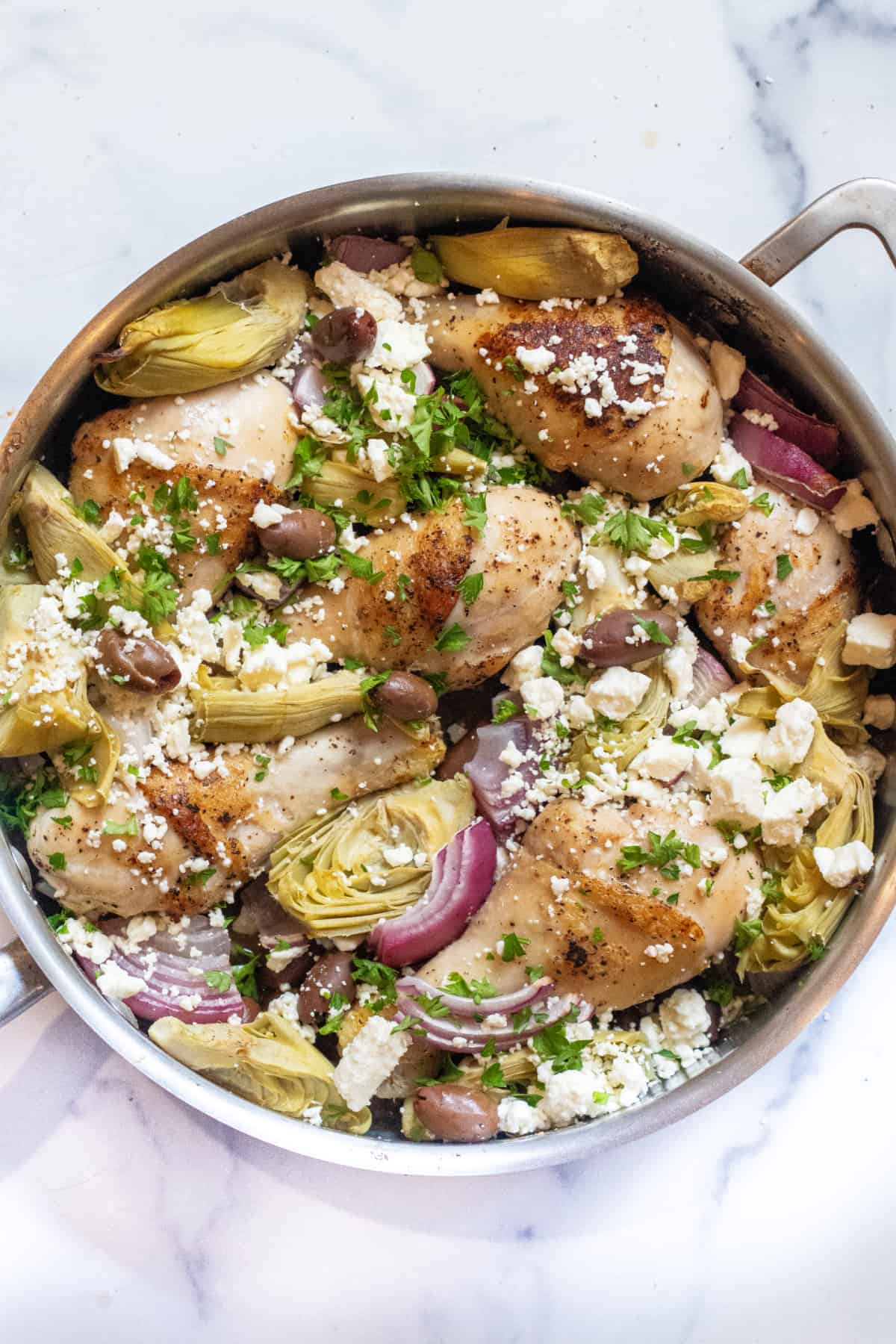 a pan of chicken legs, olives, artichokes, and feta cheese.