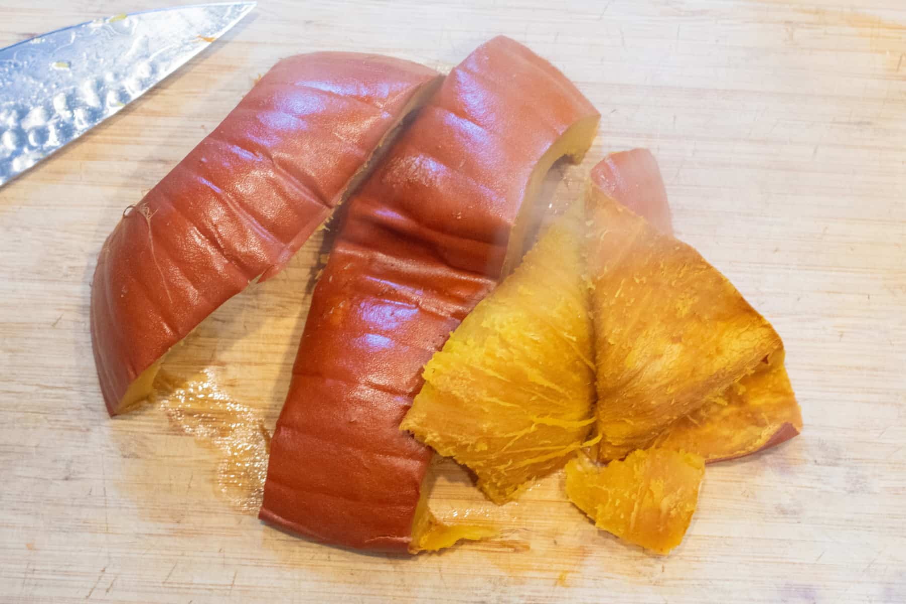 cut and roasted pumpkin on a cutting board with the skin being pulled off. 