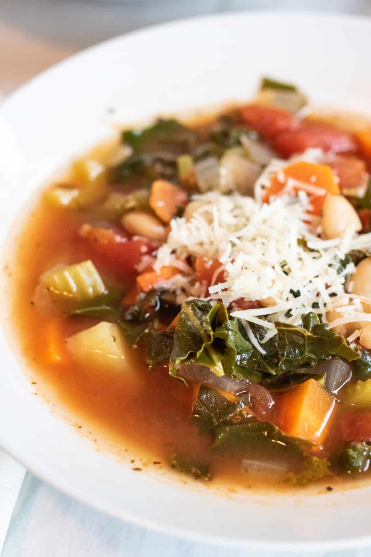 an overhead of a bowl of soup with kale, potatoes, beans, and carrots topped with cheese.