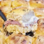 a slider with ham and bechamel sauce being held up in a pan of them.
