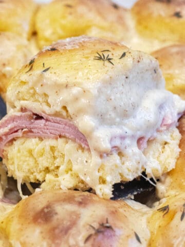 a slider with ham and bechamel sauce being held up in a pan of them.