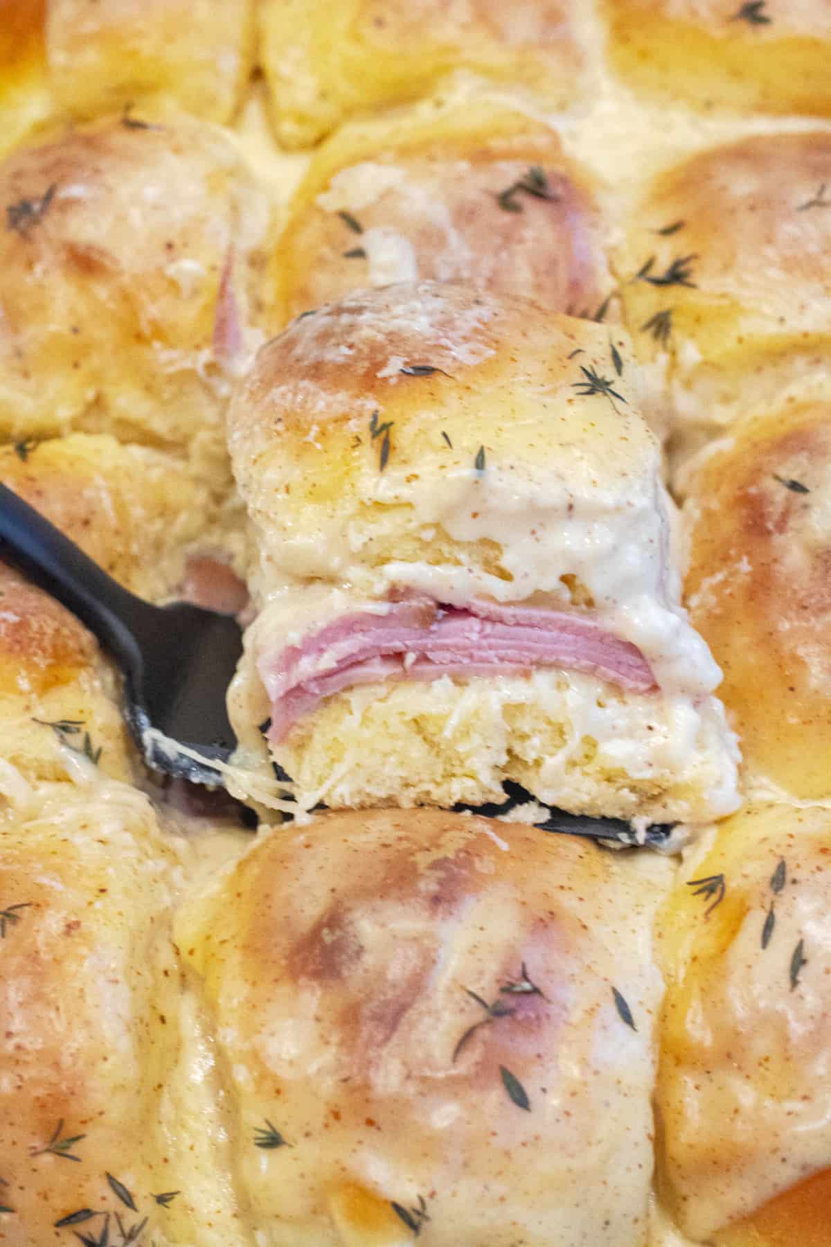 a slider with ham and bechamel sauce being held up in a pan of them.