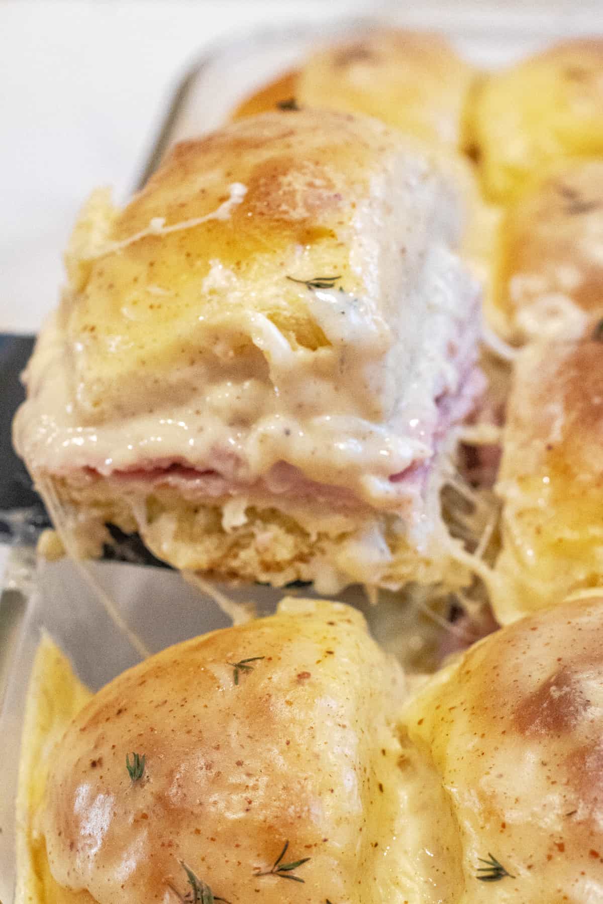 a slider with ham and bechamel sauce being held up in a pan of them.