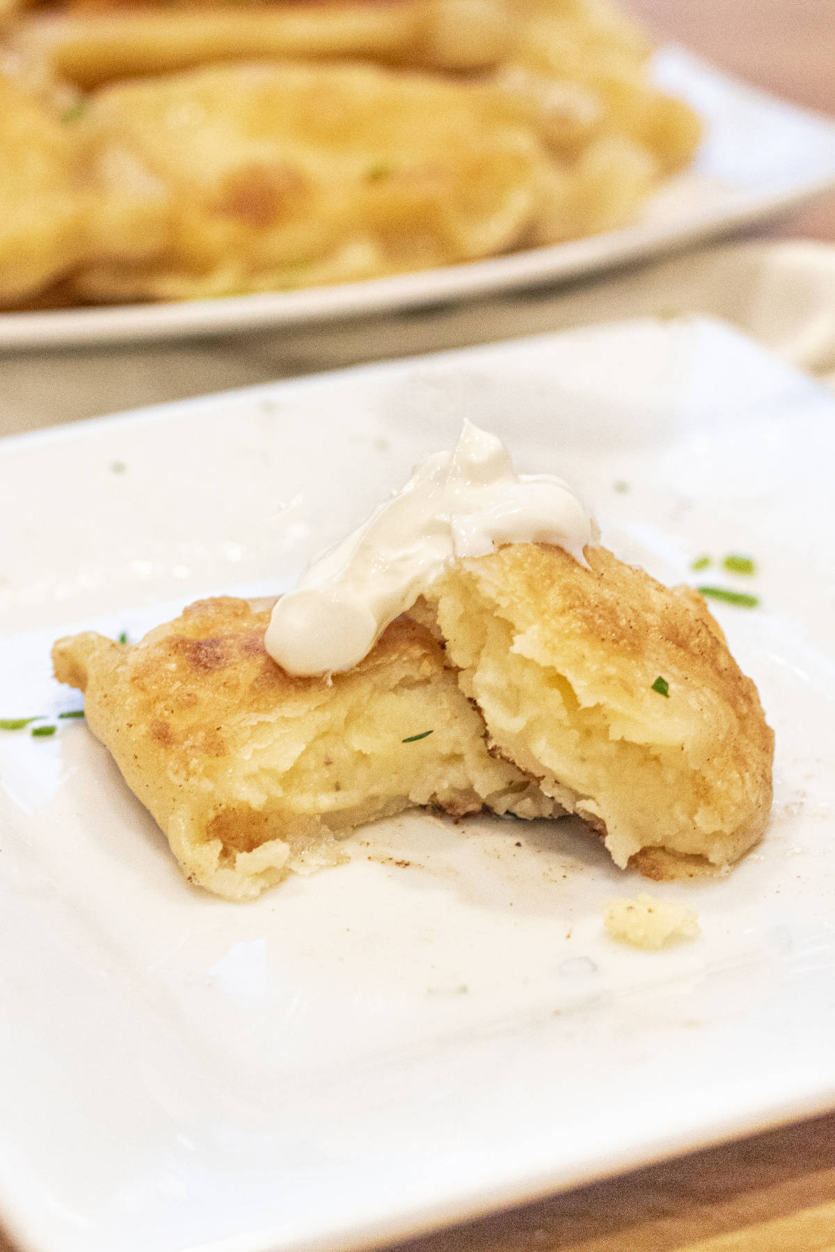 a potato pierogi on a plate in half with a dollop of sour cream.