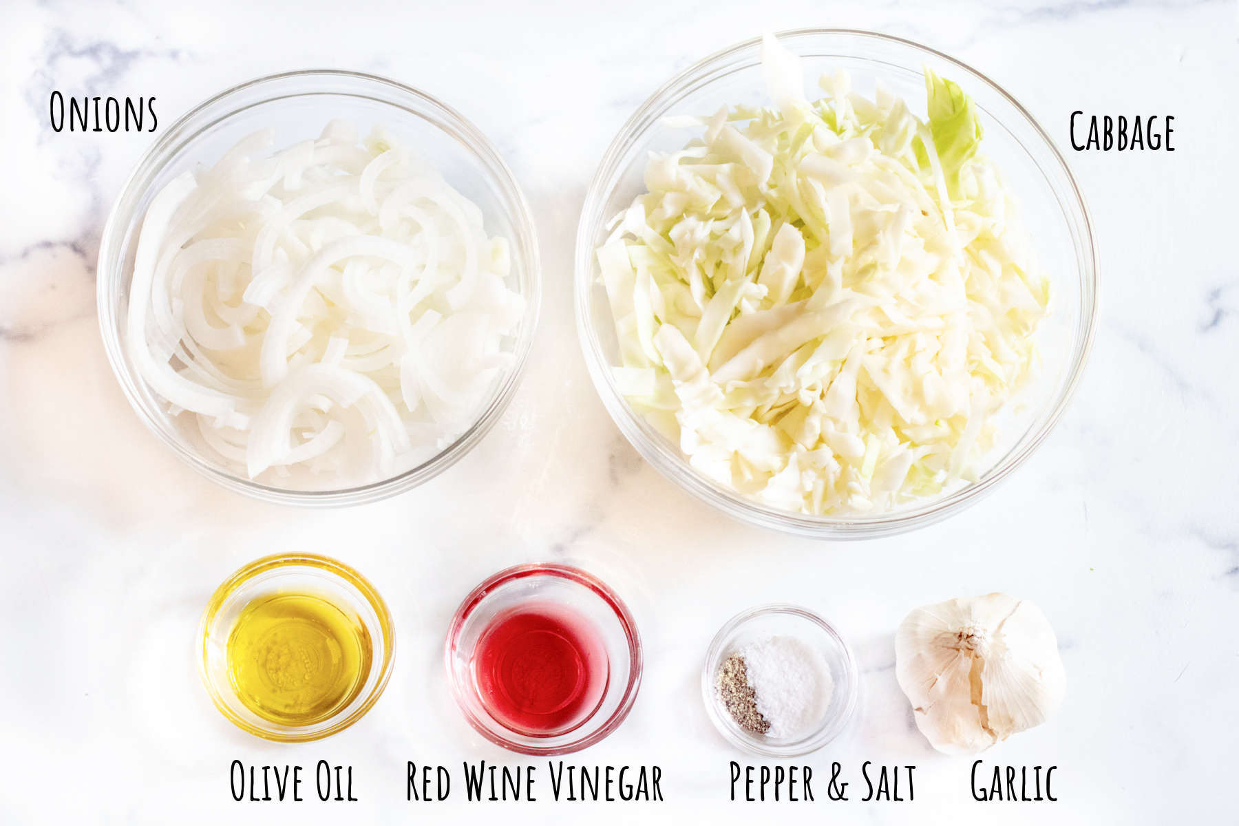a bowl of sliced onions, cabbage, and bowls of oil, vinegar, salt and pepper, and garlic on a labeled counter.