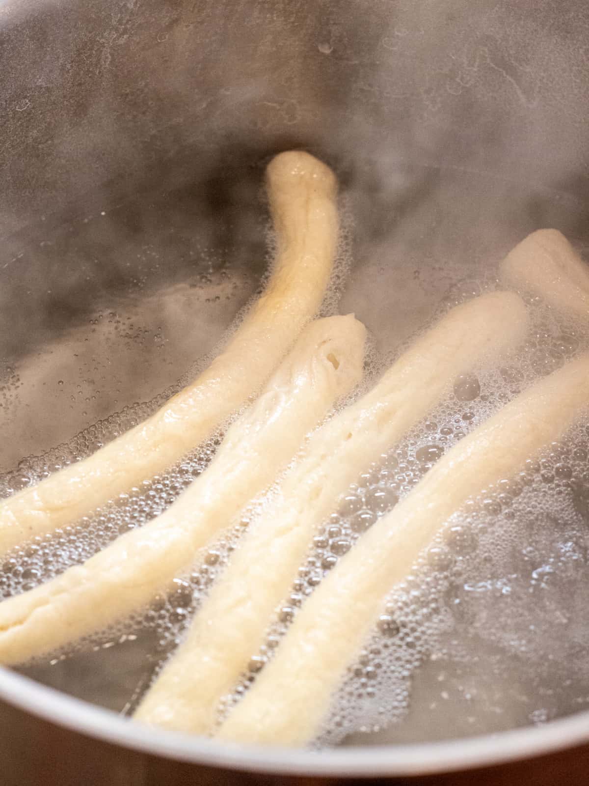 pretzel rods boiling in water in a pot.