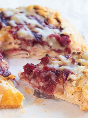 a slice of a cranberry, turkey, mashed potatoes and gravy galette with a slice being take out.