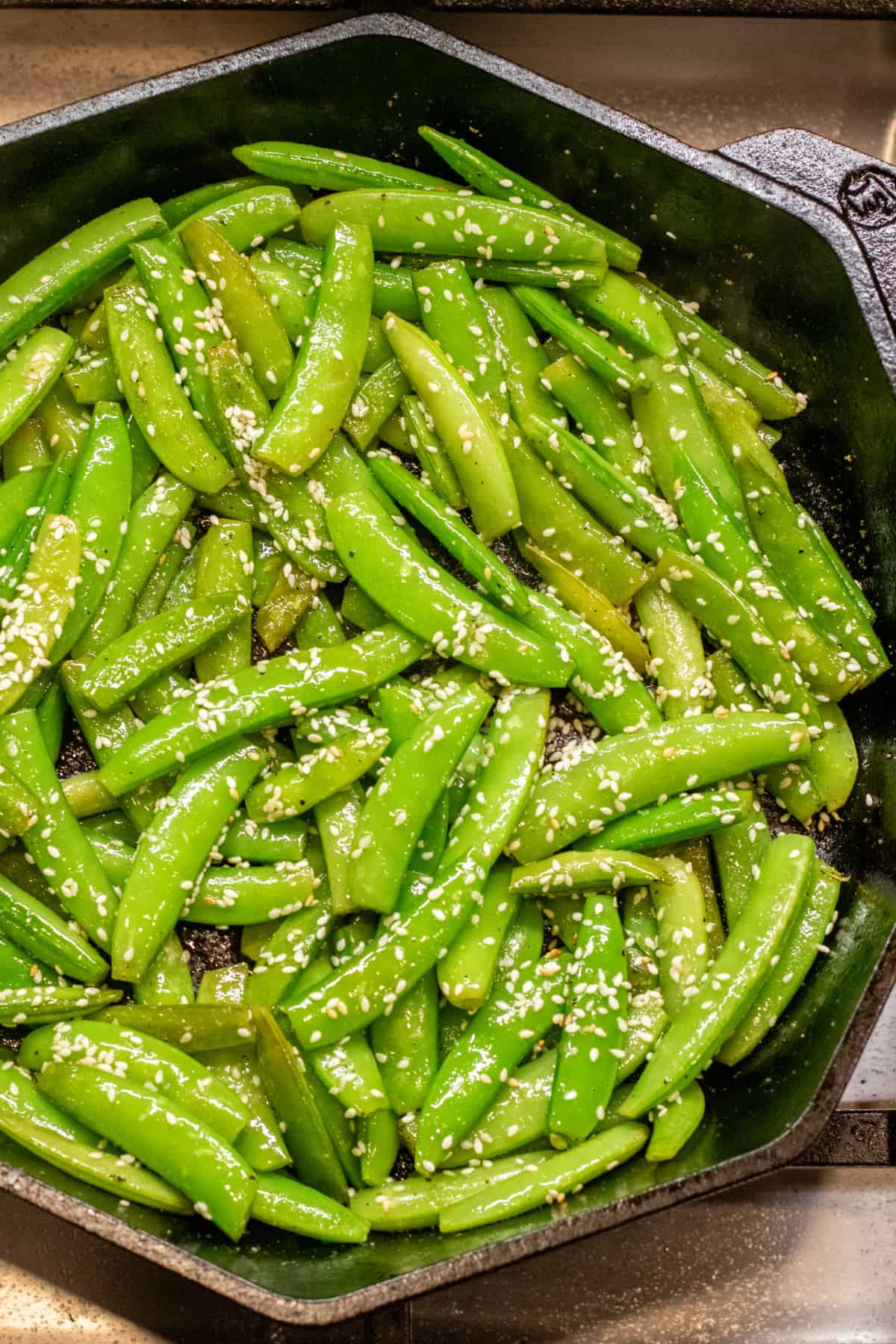 a cast iron of sauteed sugar snap peas topped with sesame seeds.