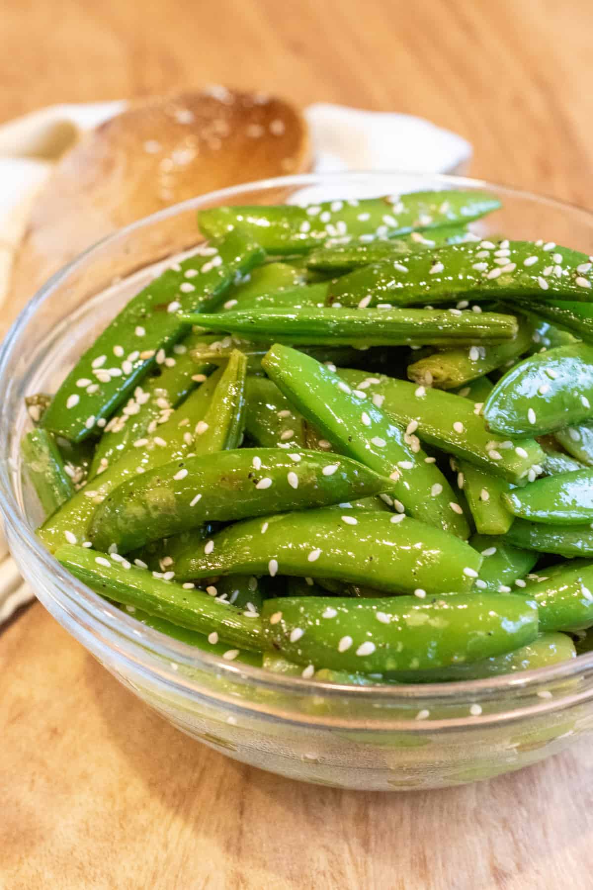 a bowl of sesame seed covered cooked sugar snap peas.