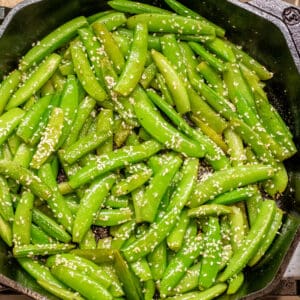 a cast iron of sauteed sugar snap peas topped with sesame seeds.