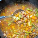 a dutch oven of beef and vegetable soup with a ladle in it.