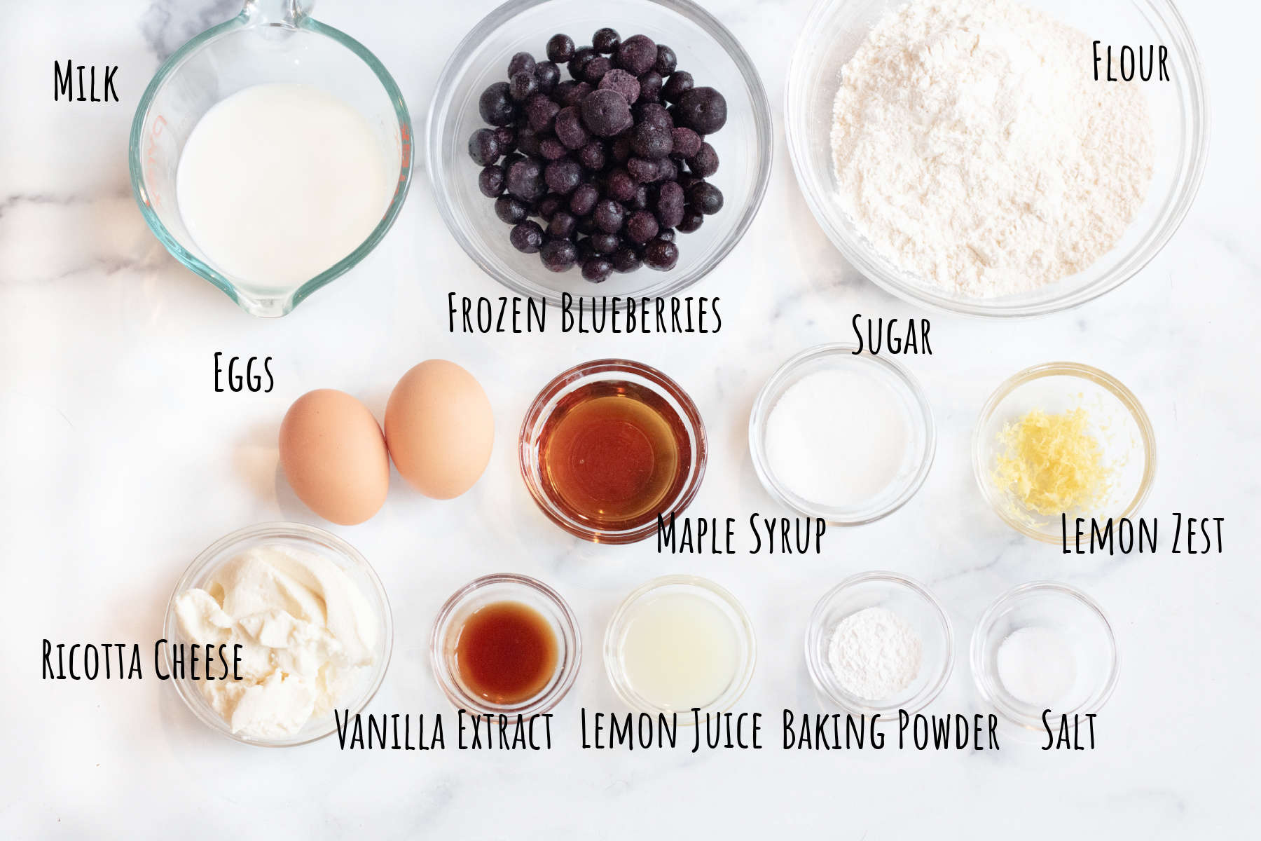 milk, frozen blueberries, flour, eggs, maple syrup, vanilla, lemon zest, vanilla, ricotta, baking soda, salt, eggs, all on a counter.