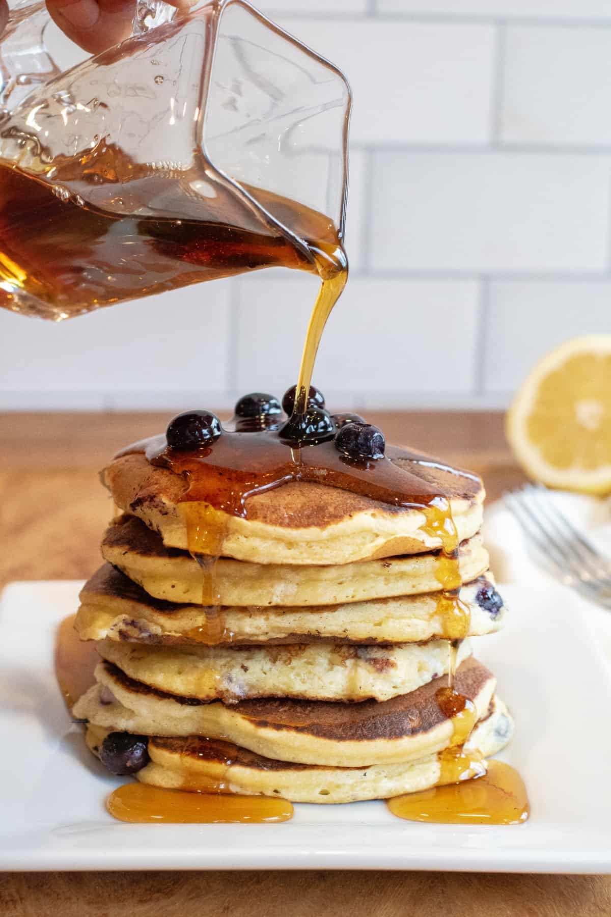 a stack of pancakes with blueberries and syrup being poured over it.