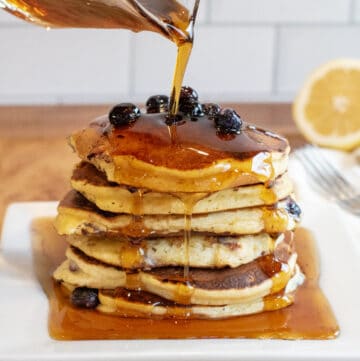 a stack of pancakes with blueberries and syrup being poured over it.