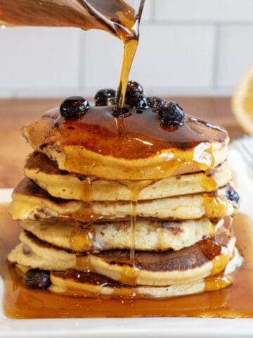 a stack of pancakes with blueberries and syrup being poured over it.
