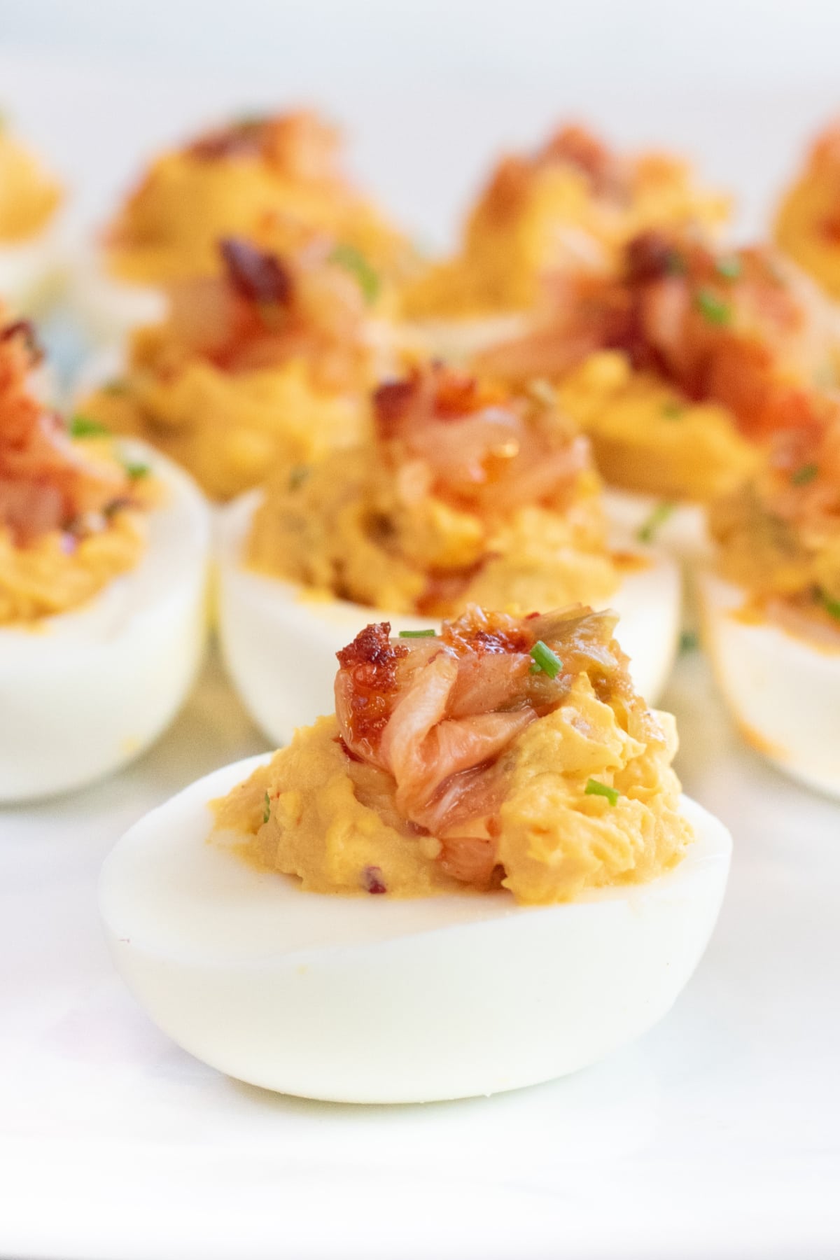 a plate of deviled eggs with kimchi on the top.