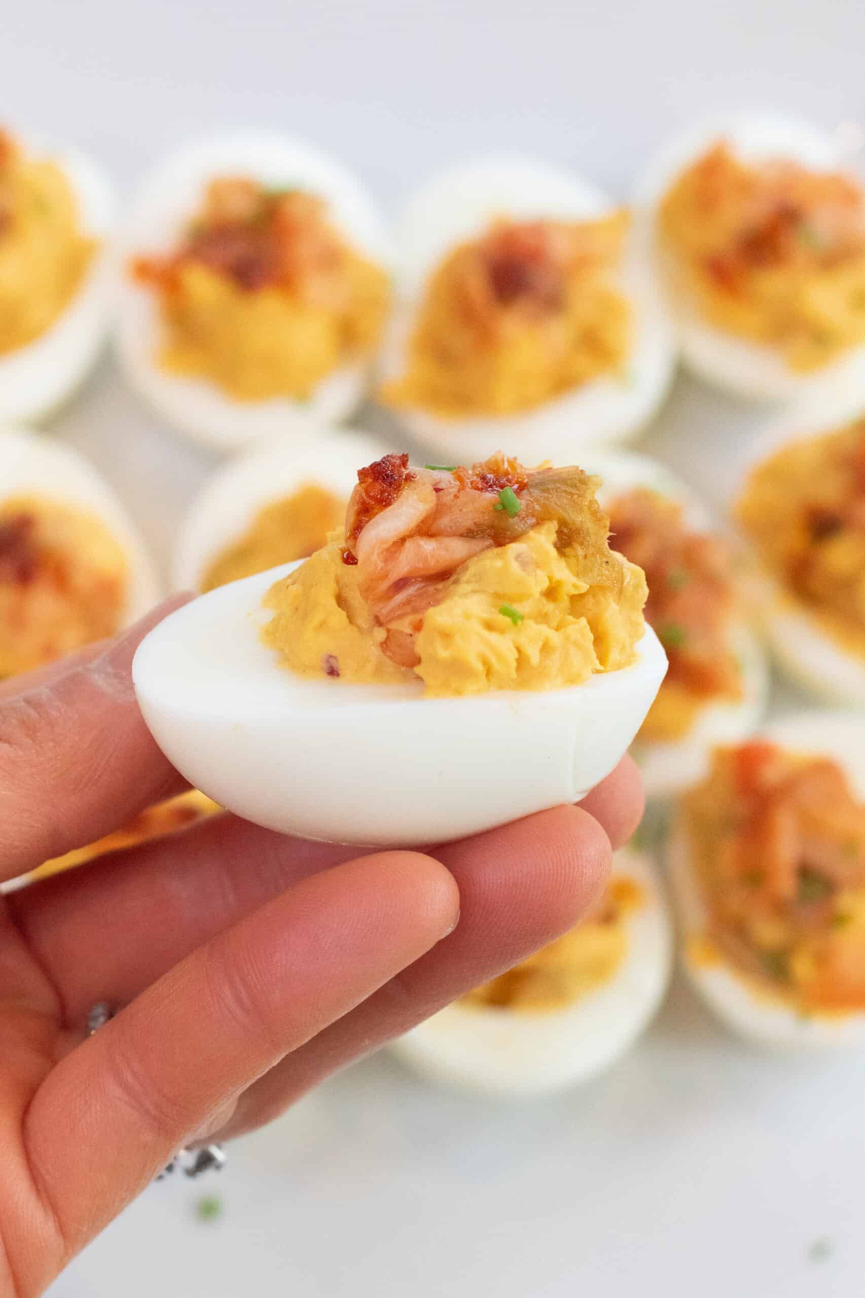 a hand holding a deviled egg topped with Kimchi. 