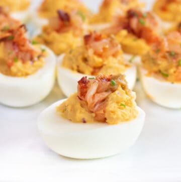 a plate of deviled eggs with kimchi on the top.