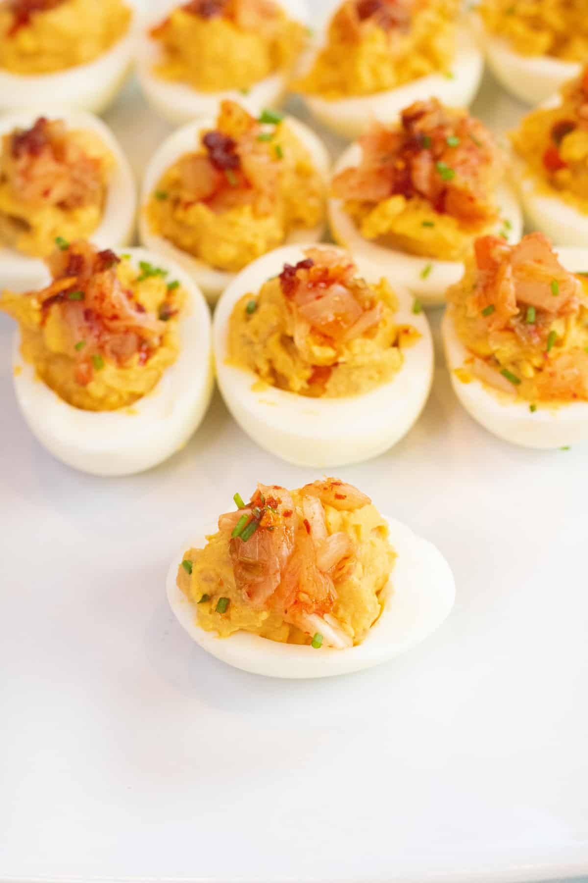 a plate of deviled eggs with kimchi on the top.