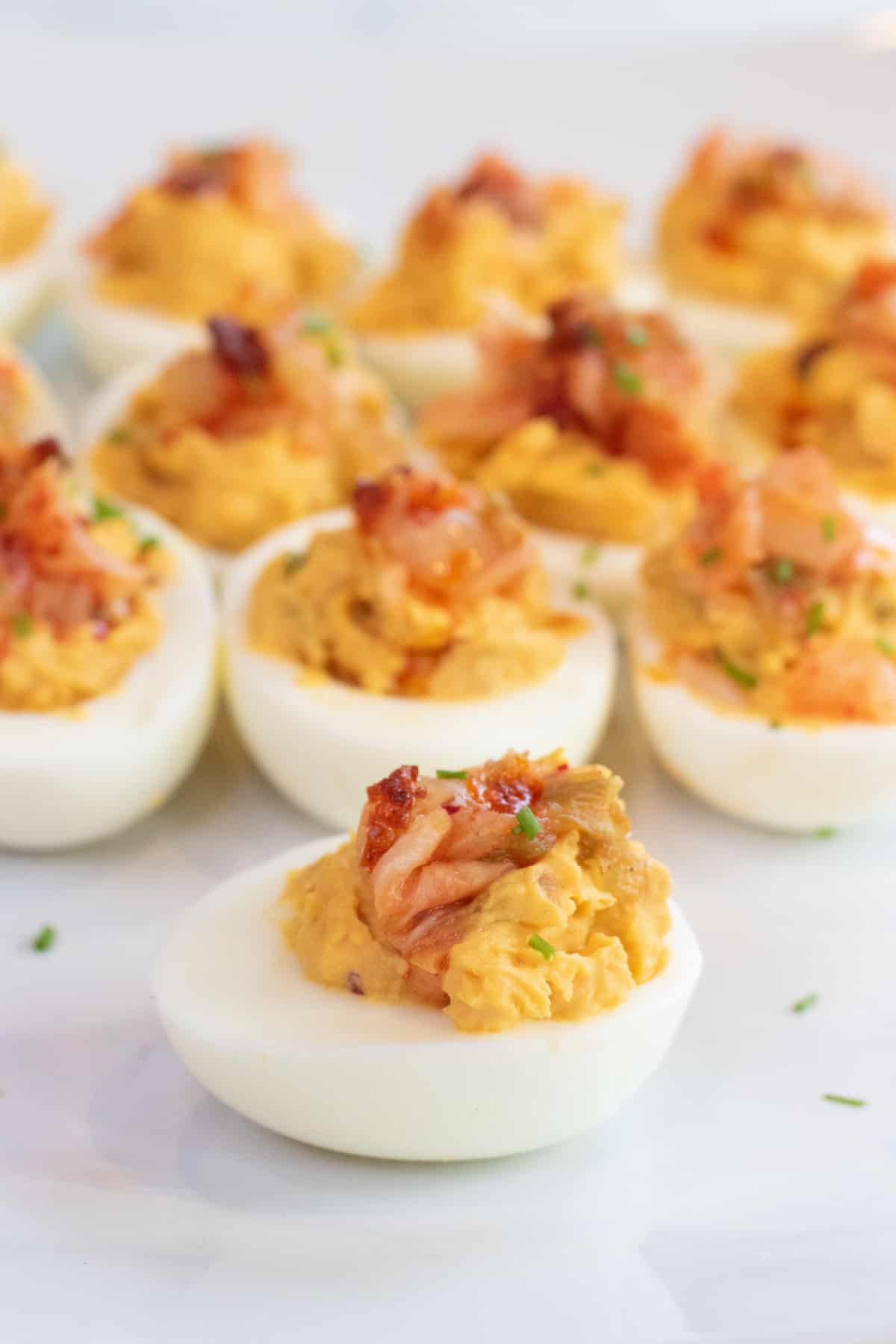 a plate of deviled eggs with kimchi on the top.