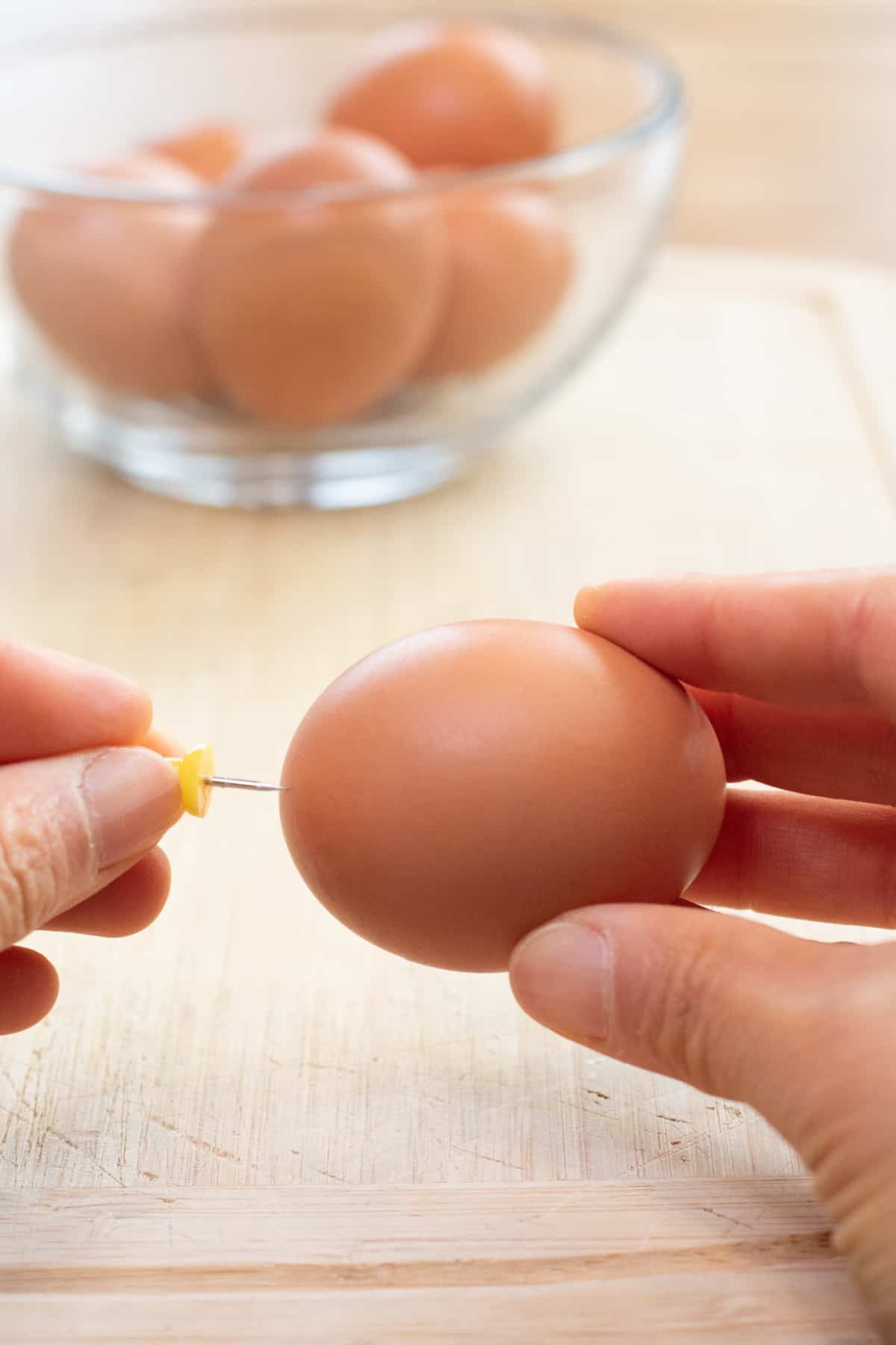 a hand pricking the end of an egg with a pushpin.