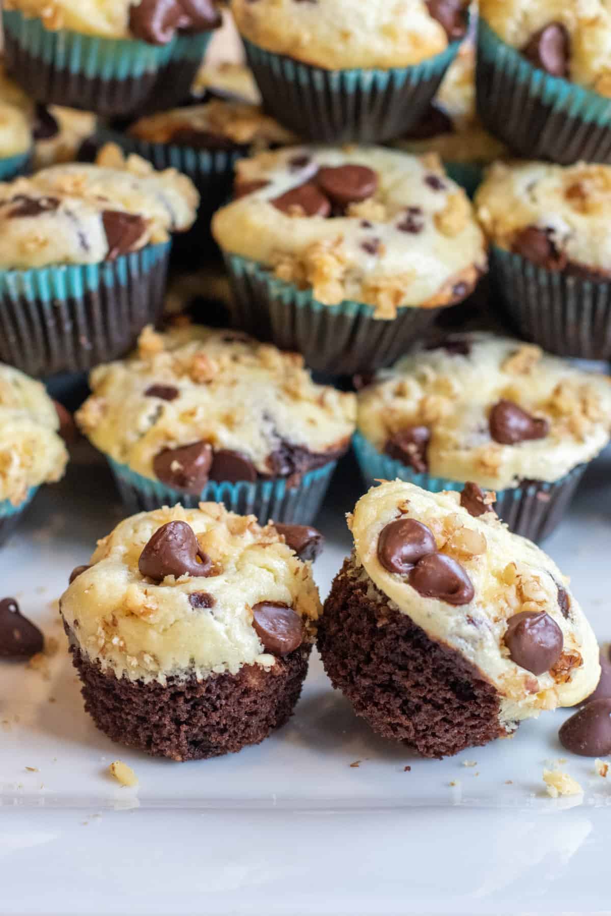 a plate of mini chocolate cupcakes with cream cheese topping and chocolate chips and walnuts on top.